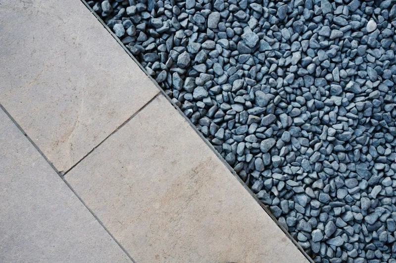 Sawn pale pavers meeting a bed of blue-grey pebbles along a clean diagonal edge, from above.