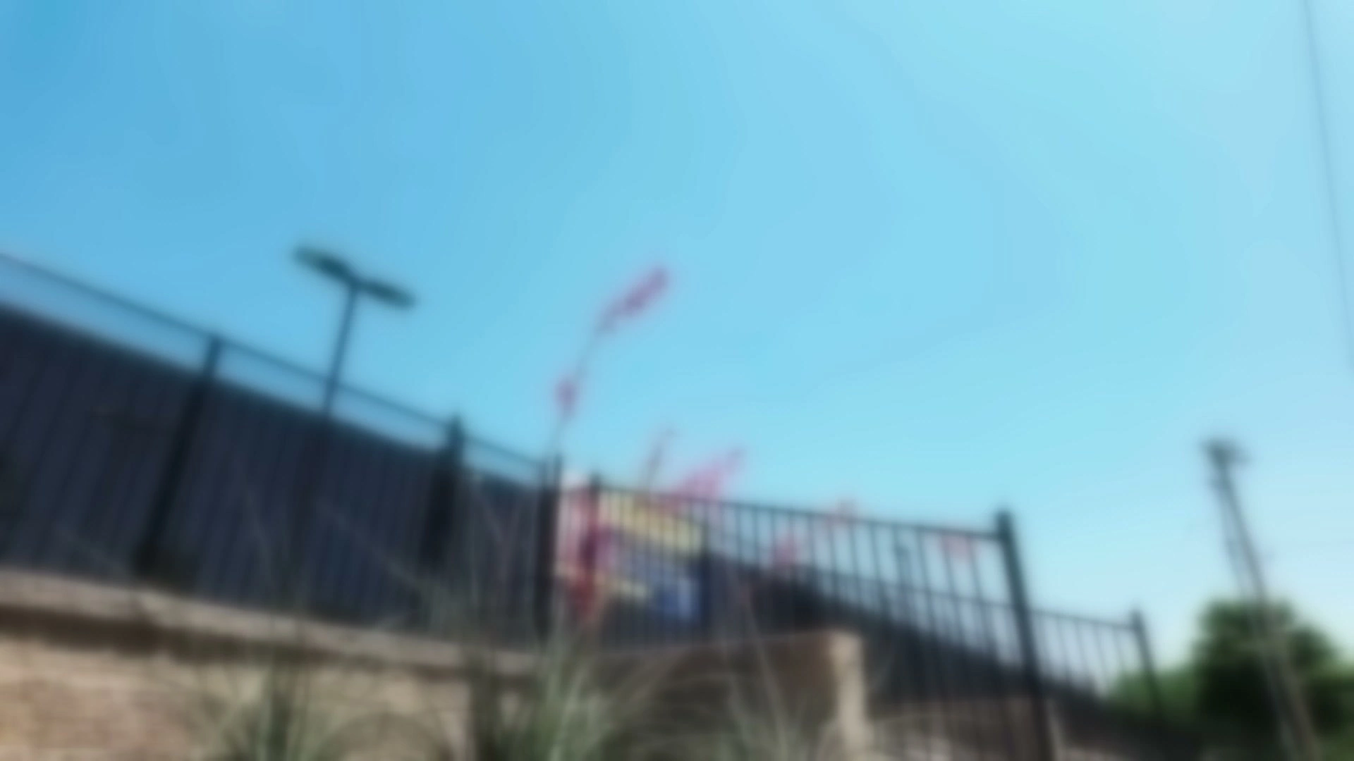 A soft-focus frame of the film behind the headline: a black iron fence on a stone retaining wall, red flowering yucca, and a paver walk in bright sun.