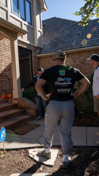 Three of the crew at a client's front steps, one pointing out the bed line to the other two.