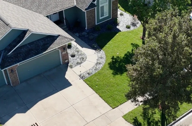 A finished frontage from above: new white-rock beds along the house and walk, fresh sod and the drive, with the shade tree kept.
