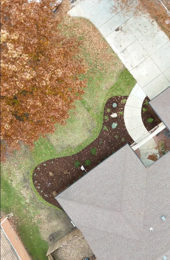 A tall overhead frame of the finished bed running the length of the frontage, with the drive and an autumn maple at the top of the shot.