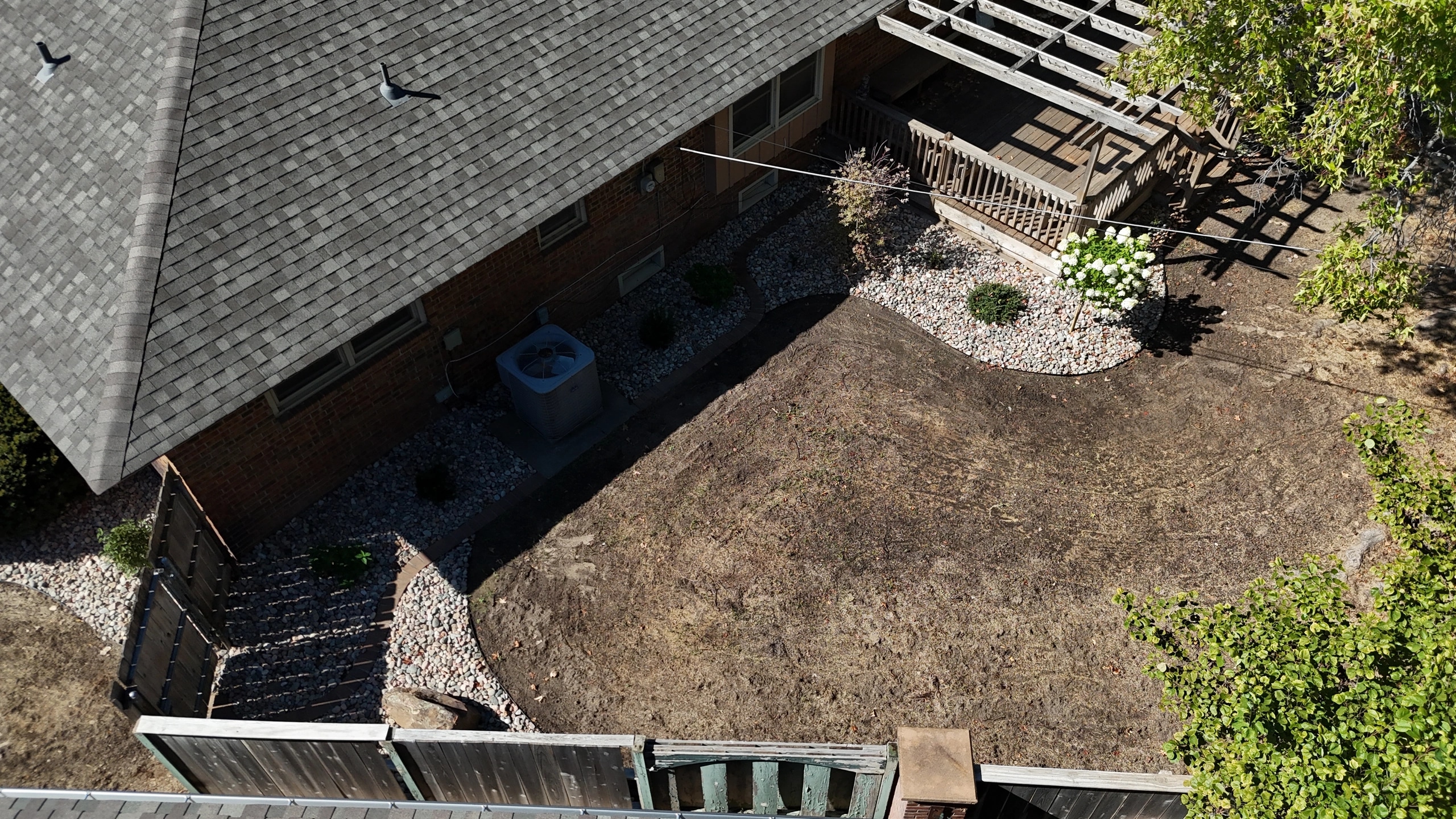 The same side from above after the work: the air conditioner in a clean river rock bed along the house, curving out to the deck and a tree-form hydrangea.