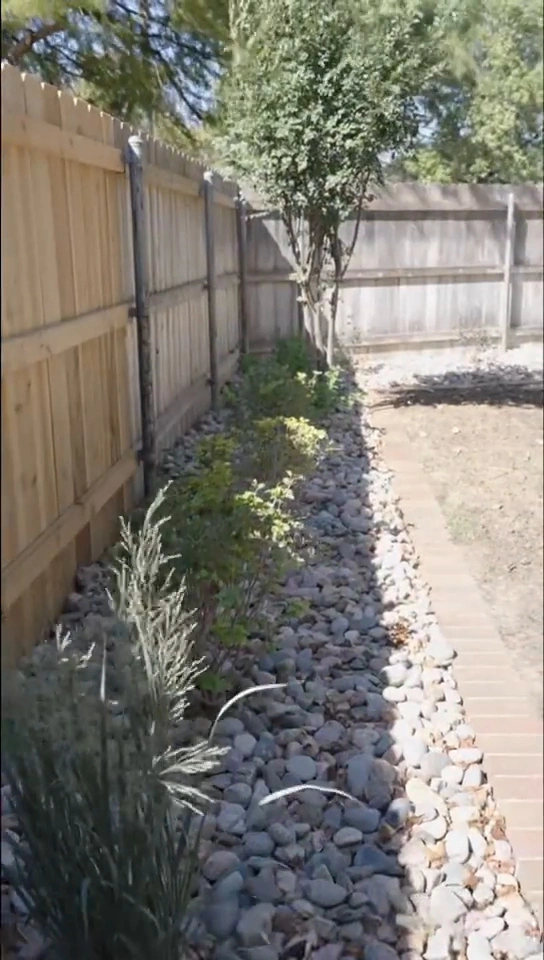 A narrow river rock bed along the side fence of the Brown residence, planted with ornamental grasses and shrubs beside a brick walk.