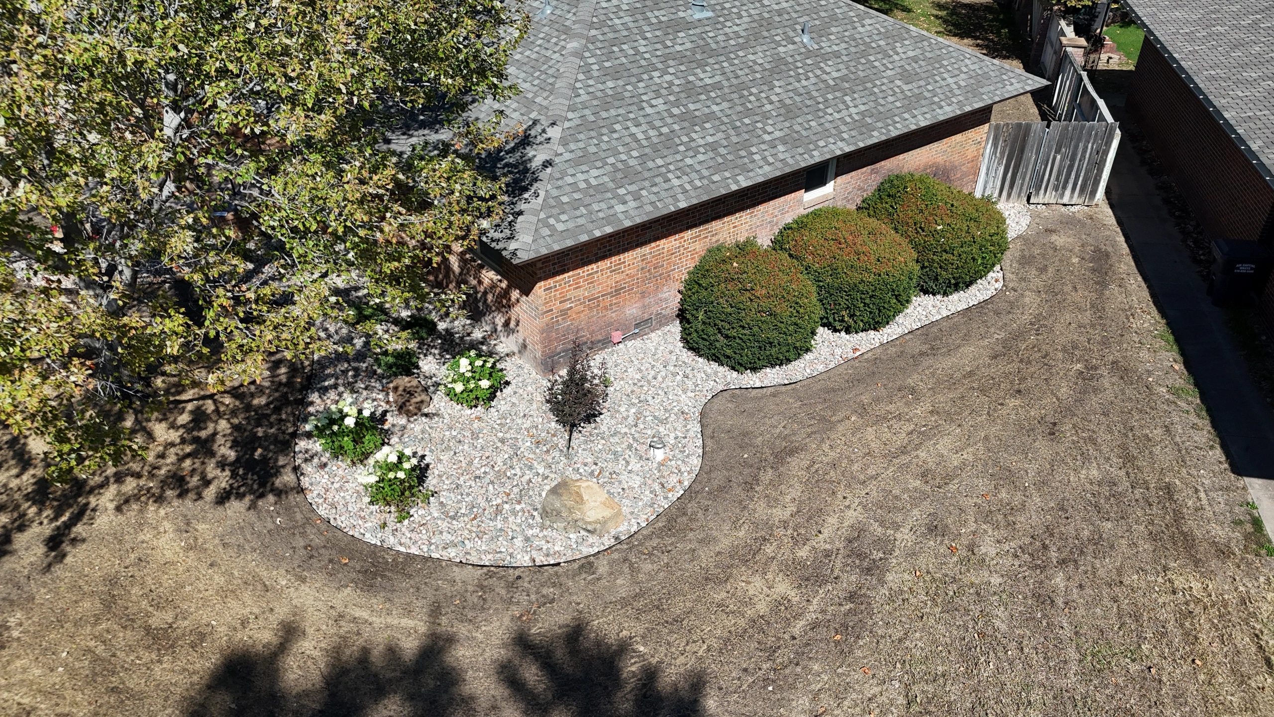 The Brown residence from above: river rock beds edged in black curving along the house, with rounded evergreens, hydrangeas and a boulder.