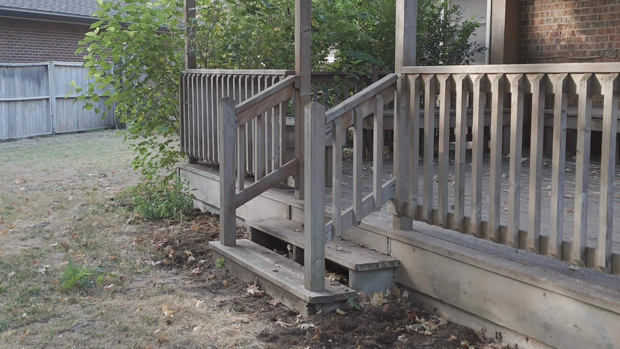 The back deck of the Brown residence before the work: bare dirt and straggling growth along its foot, and a thin lawn running up to the steps.