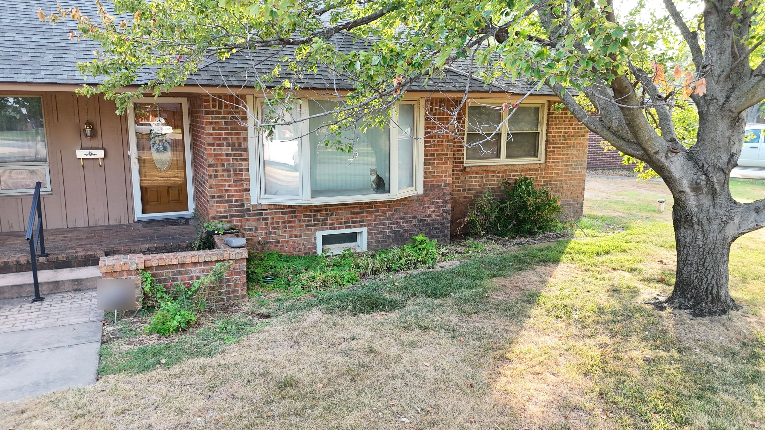 The front of the Brown residence before the work: a foundation bed of weeds and straggling shrubs under the bay window, and a patchy, dry lawn.