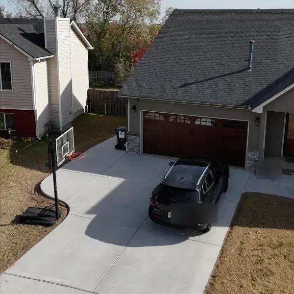 The new drive from above with the car parked on it and the basketball hoop at its edge, the side yard and fence beyond.