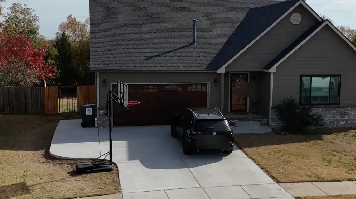 The Debroata house and new drive from above the street: the basketball hoop at the drive’s flared edge, fresh sod strips and the fenced yard behind.