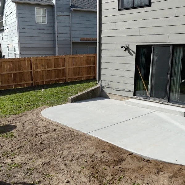 The new rear patio slab poured and floated up to the house, with the cedar privacy fence closing the boundary behind it.