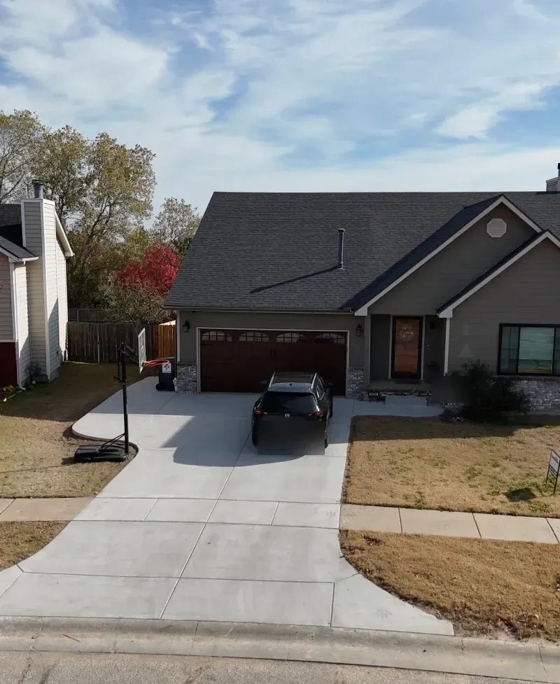 The Debroata frontage from the street: the new full-width concrete drive and walk, the car parked on it, the lawn edges cut in either side.