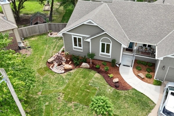 The Graber frontage from above: new sod laid in strips, a boulder-and-rock bed at the corner of the house and a curved mulched bed along the walk.