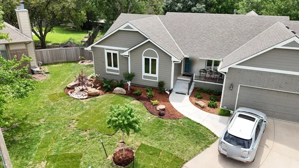 The front of the Graber residence: one curving mulched bed along the house to the porch, a Japanese maple among boulders at the corner and a young maple staked in the lawn.