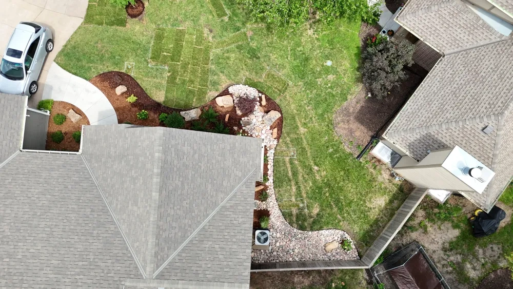 Straight down on the Graber front walk: mulched beds on both sides of it with boulders and new shrubs, fresh sod in the lawn and a young tree in a mulch ring.