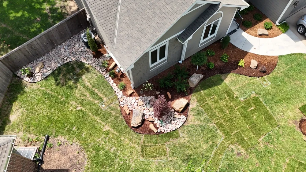 From above the Graber front corner: river rock and boulders running along the side of the house into the mulched front bed, with fresh sod squares in the lawn.