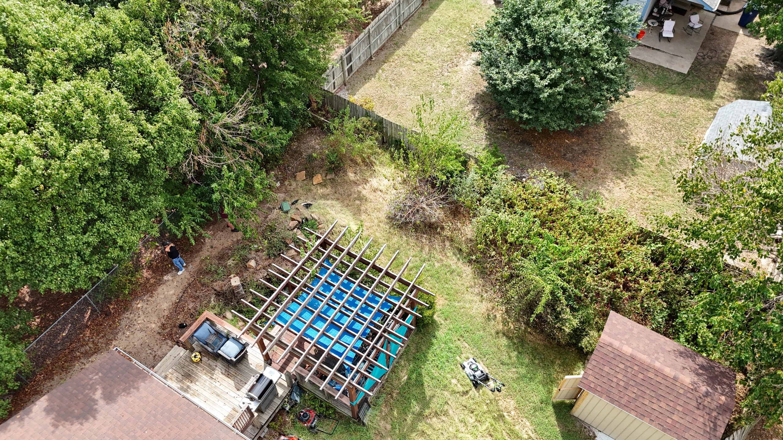 The back yard from above before the cleanup: brush and saplings spilling off the fence lines around the pergola deck, the pond and a weedy lawn.
