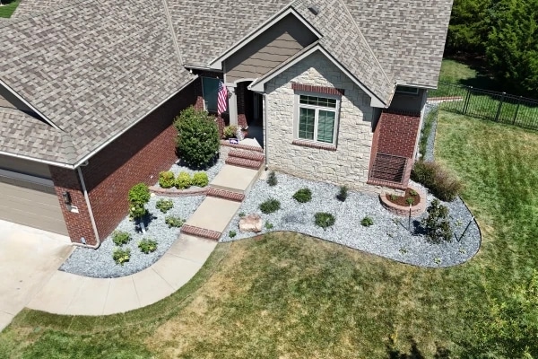 The Kellie stone-and-brick frontage from above, white rock beds either side of the walk and the flag by the door.