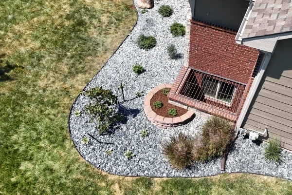 White rock beds wrapping a brick window well from above, with a curved brick-edged planter and young shrubs set through the rock.