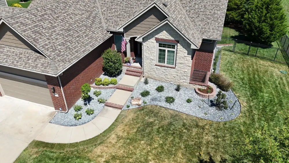 The Kellie frontage from above: grey rock beds wrapping the stone-and-brick entry, young shrubs spaced through them and the walk curving down to the drive.