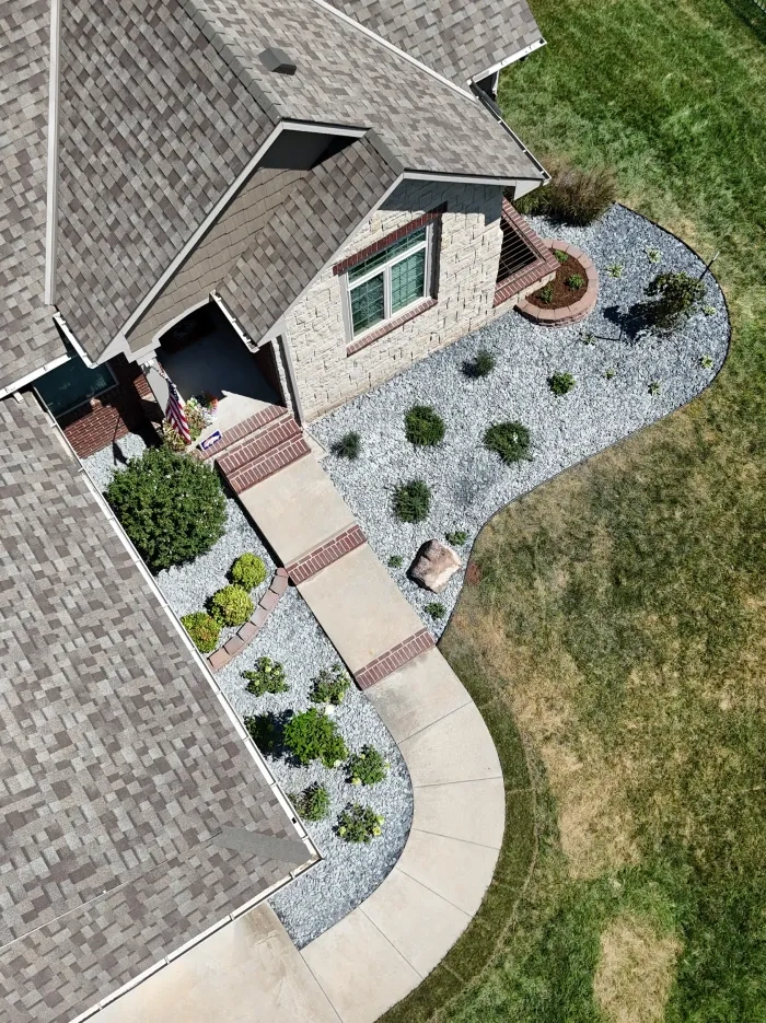 An overhead view of the Kellie Residence, where a curving concrete walkway and brick-edged steps run between grey gravel beds planted with clipped shrubs and grasses.