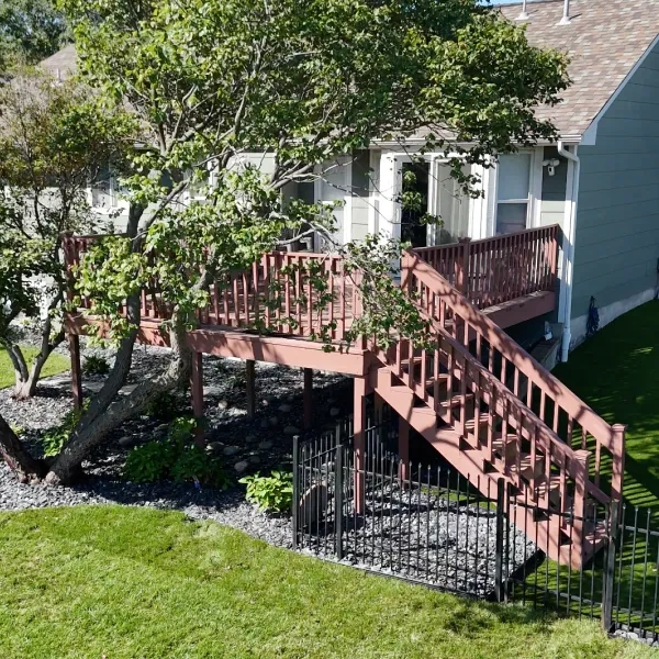 The Kumar Residence deck stairs after the renovation, with a decorative iron rail, a slate rock bed beneath and new planting along the lawn edge.
