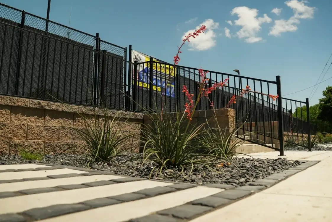 Paver stepping stones set into decorative aggregate beside the courts, with red flowering yucca and ornamental grasses along a segmental retaining wall.