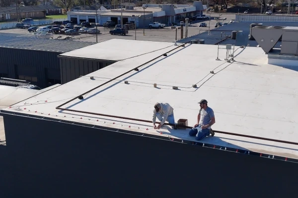 Two Earthworks crew members kneeling on the flat commercial roof at Rhoden Roofing, fixing a lighting run along the parapet in daylight.