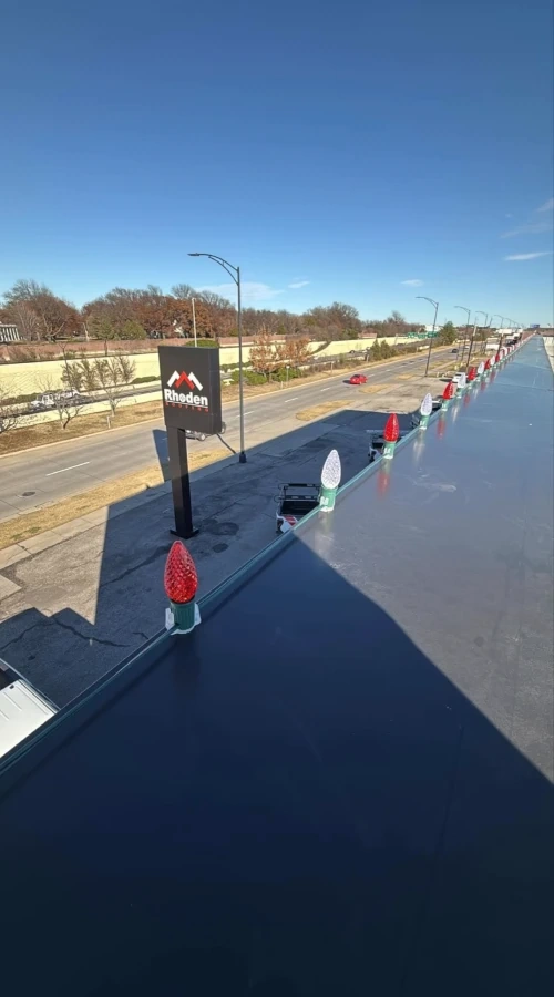The Rhoden roof edge from above with red and white C9 bulbs going on along the parapet, the Rhoden sign and the highway below.