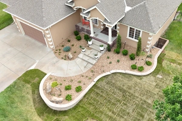 The Riley frontage from above: a curved seat wall holding a gravel bed of new plantings, the steps and porch behind and fresh sod beyond.