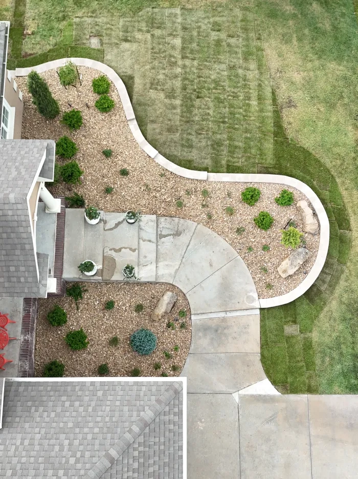Straight down on the Riley entry: the capped block wall curving around a decorative rock bed of evergreens and boulders, the steps and walk, and new sod beyond.