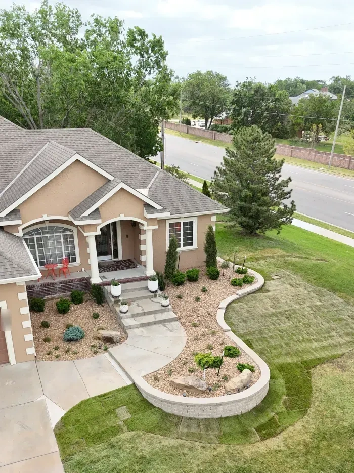 The Riley residence from above the lawn: the raised block planter, the curving rock bed along the house with columnar junipers, and the street and trees beyond.