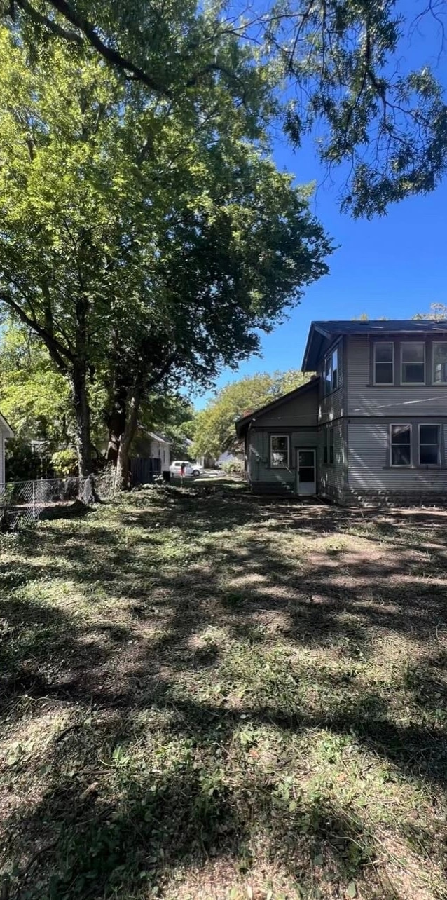 The same back yard cleared to open ground under the mature trees, the whole back of the house in view.