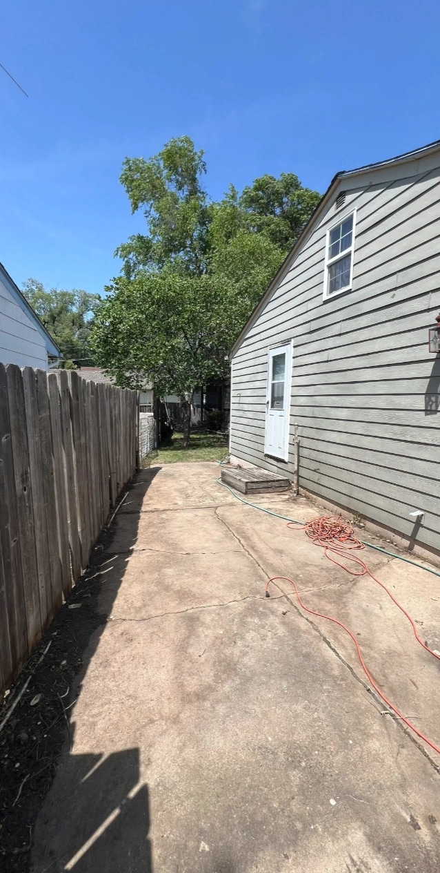 The same side yard cleared to bare paving from the fence to the house, the back door and step in the open.