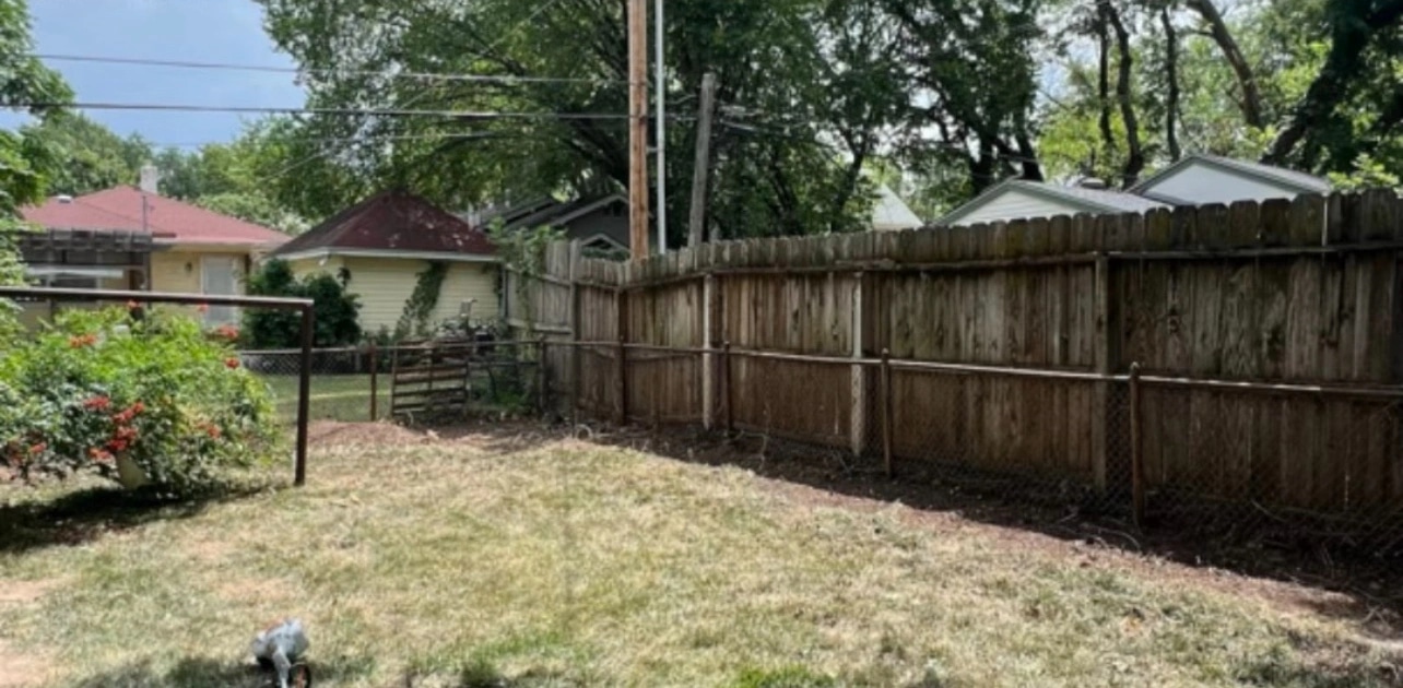 The same fence line cleared back to the boards, the whole run of fence visible along the edge of the lawn.