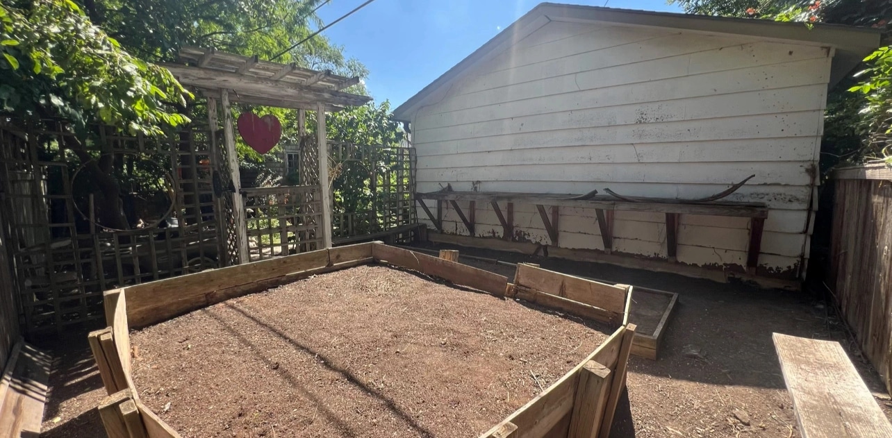 The same raised beds cleared down to bare soil, the debris gone and the shed wall behind them clear.